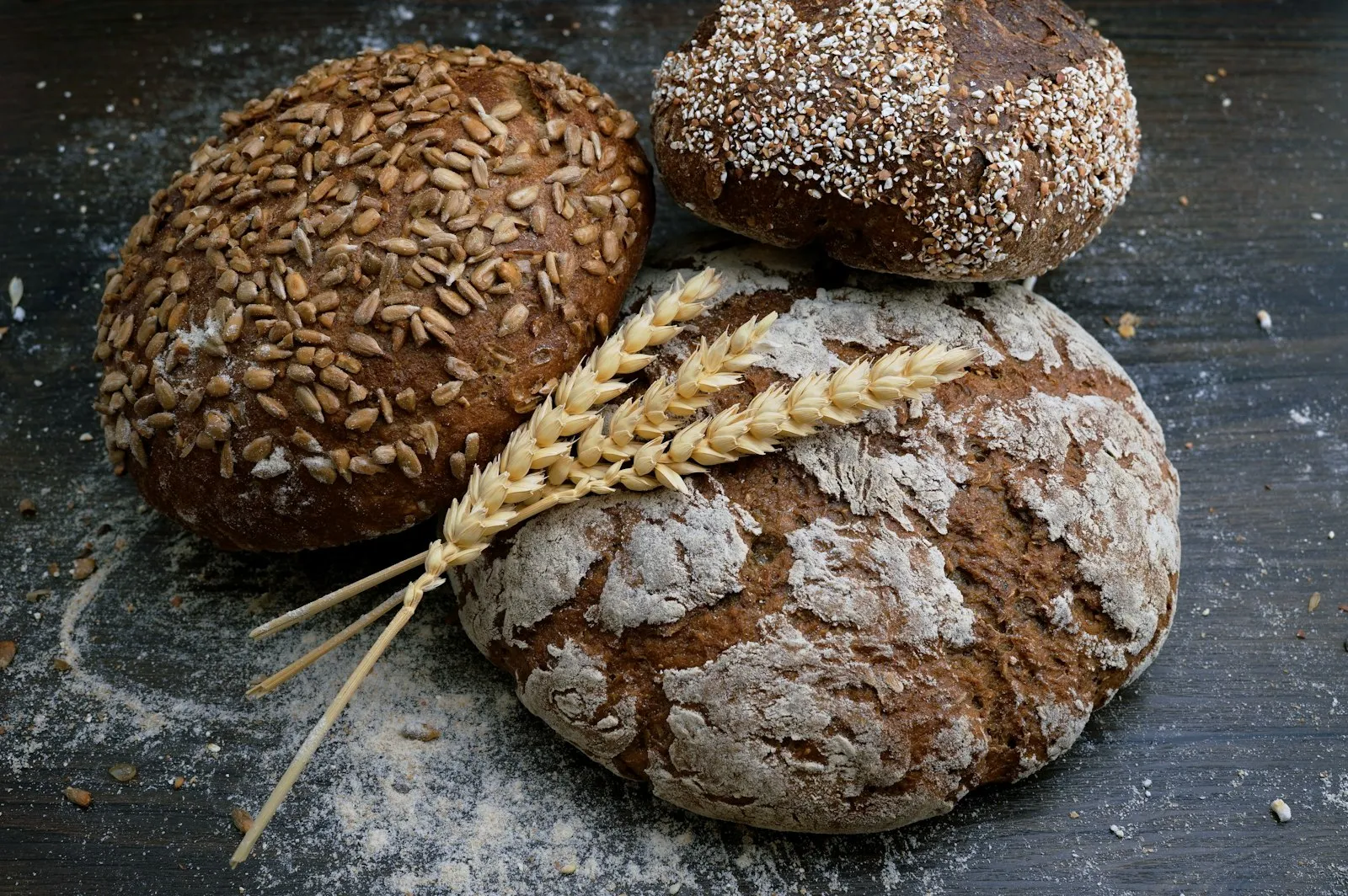 Three round loaves dusted with flour beside a sheaf of wheat